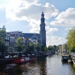 Prinsengracht canal in Amsterdam lined with gabled houses, with the Westerkerk tower rising above the trees