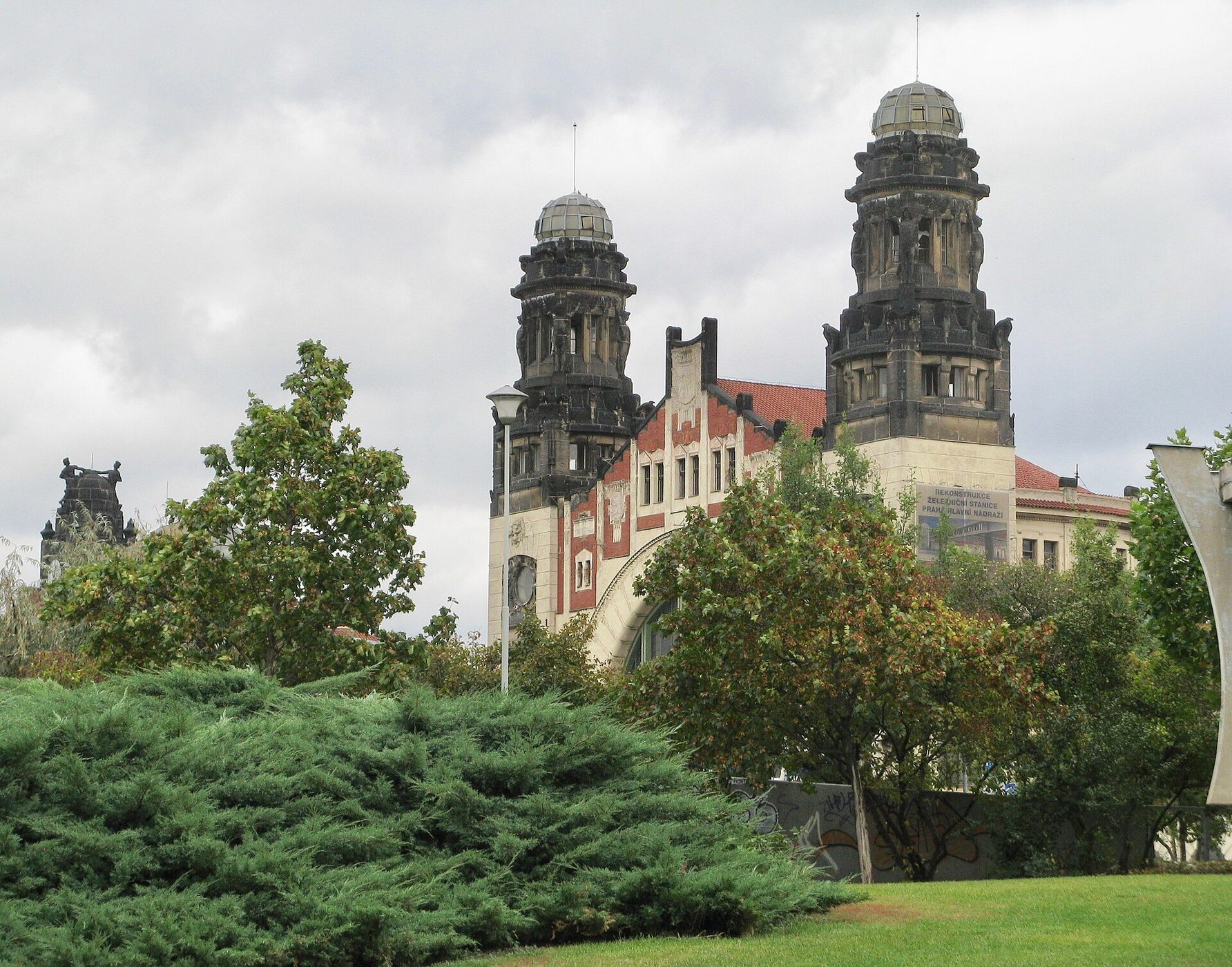 Art Nouveau towers of the Fanta Building at Praha hlavní nádraží rising above trees, near the Airport Express stop