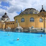The outdoor swimming pool in front of the yellow neo-baroque domed wings of Széchenyi Thermal Bath in Budapest
