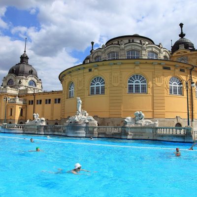 The outdoor swimming pool in front of the yellow neo-baroque domed wings of Széchenyi Thermal Bath in Budapest