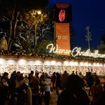 Illuminated Wiener Christkindlmarkt sign above a row of decorated stalls and crowds at the Christmas market on Rathausplatz in Vienna