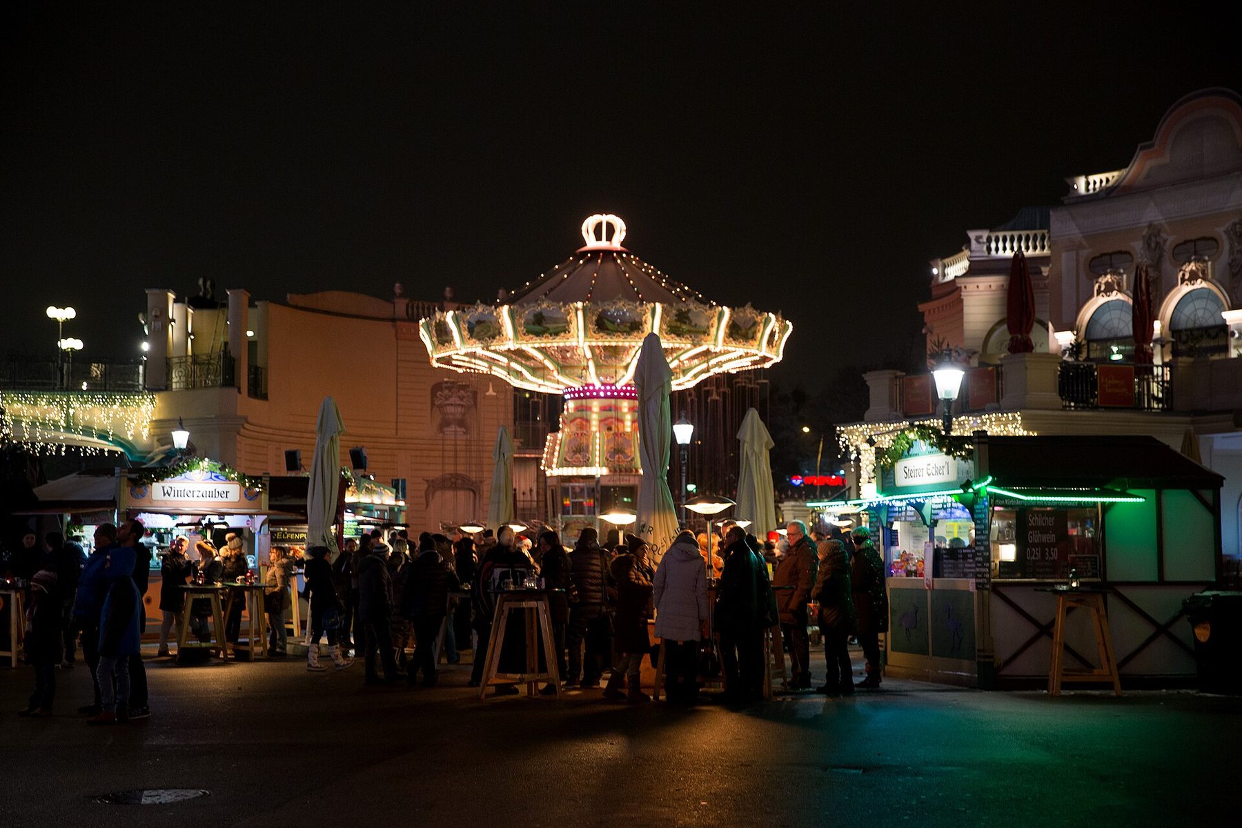 Illuminated carousel and food stalls at the Wintermarkt on Riesenradplatz in the Vienna Prater at night